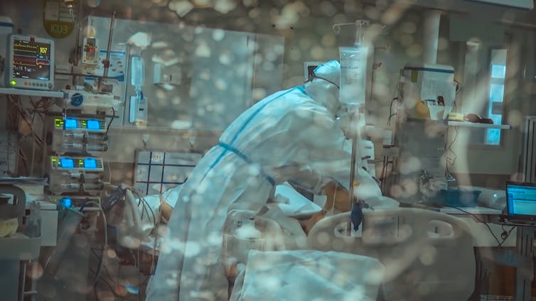 A doctor in PPE treats a COVID patient in hospital.