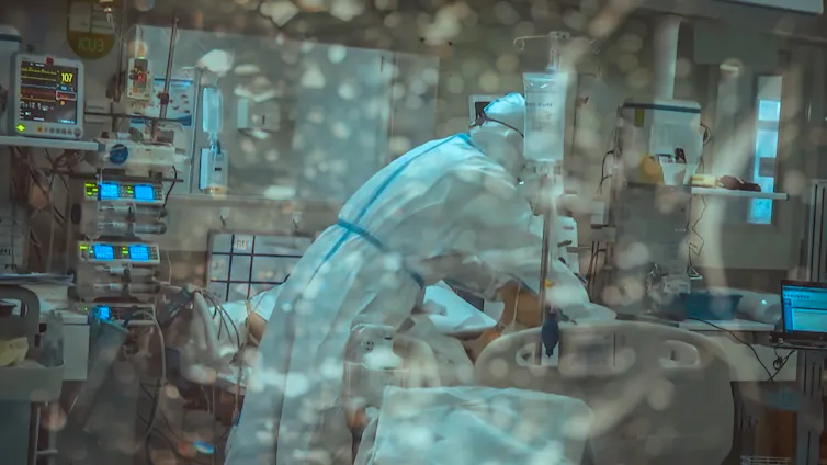 A doctor in PPE treats a COVID patient in hospital.