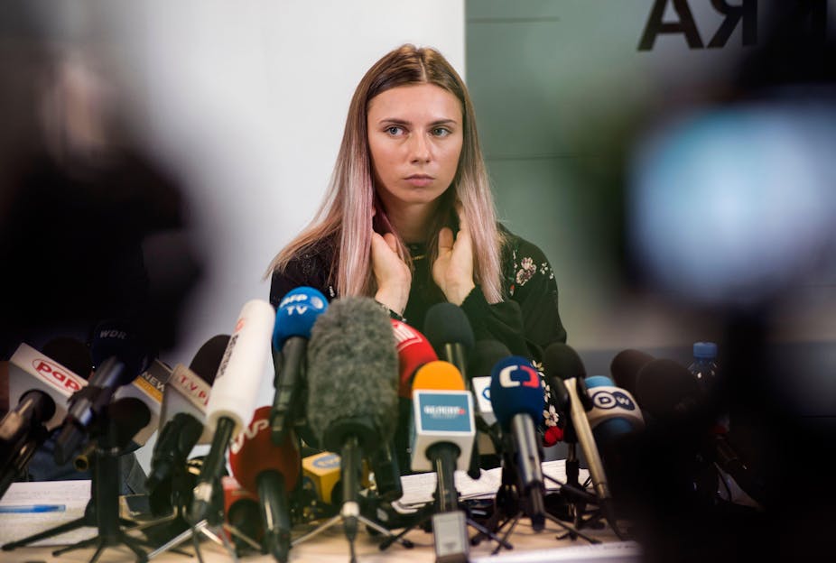 Belarusian sprinter Krystsina Tsimanouskaya seated behind a dozen or so microphones at a press conference