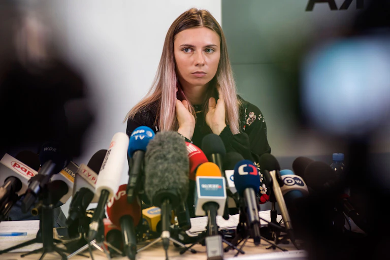 Belarusian sprinter Krystsina Tsimanouskaya seated behind a dozen or so microphones at a press conference
