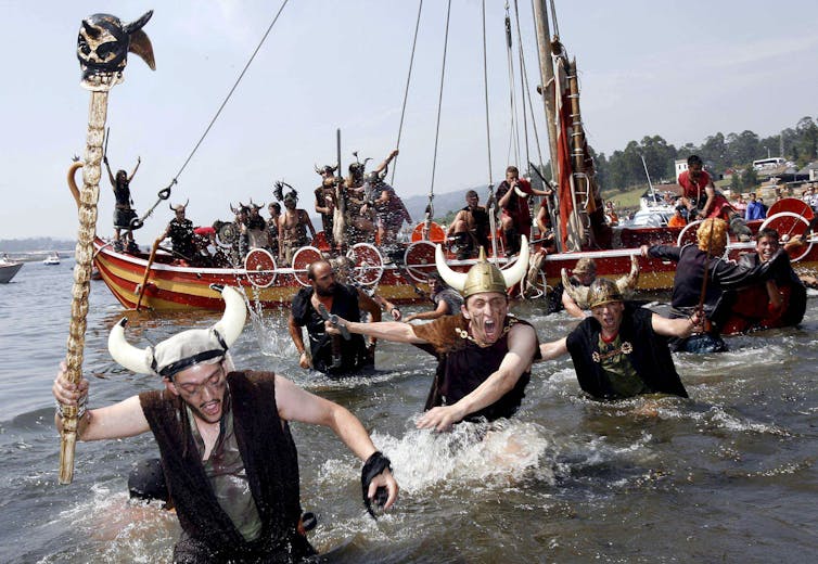 Men and women dressed as Vikings swarm ashore from a replica longship.