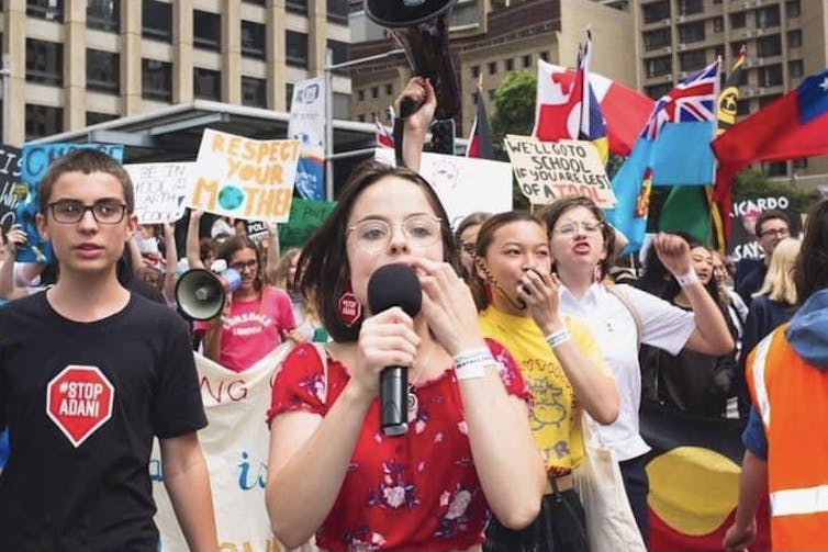 A phalanx of singing students marches towards the camera, flanked by posters and flags.