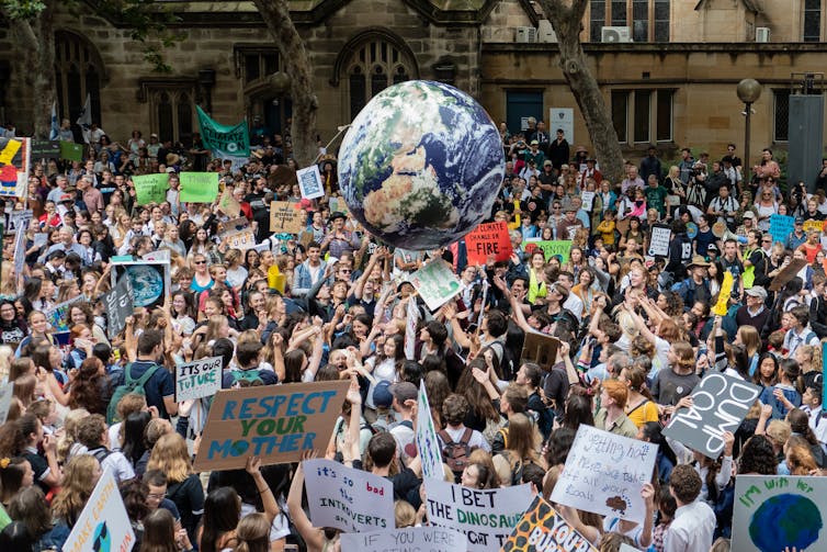 Youth strike demonstrators gather with signs and bounce an inflatable planet Earth.