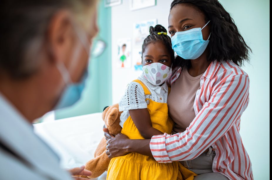 Woman wearing a face mask holding her child talking to a health care provider.