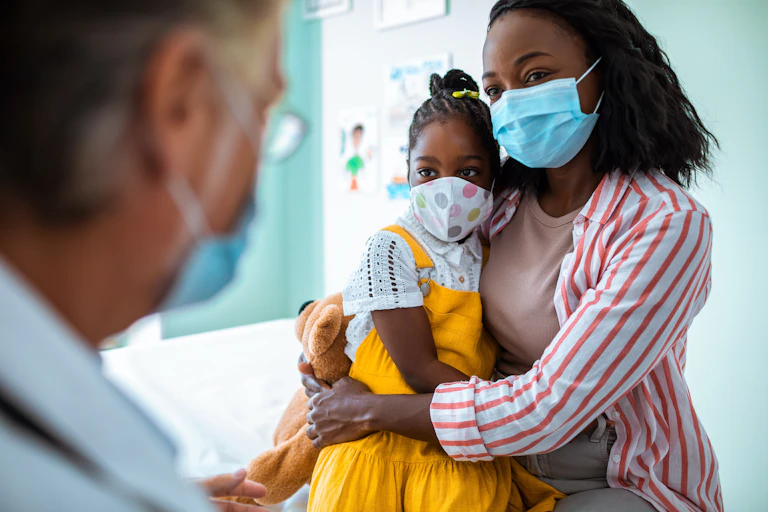 Woman wearing a face mask holding her child talking to a health care provider.