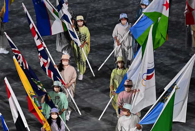 People wearing COVID masks walking into the Olympic stadium in Tokyo carrying national flags. 