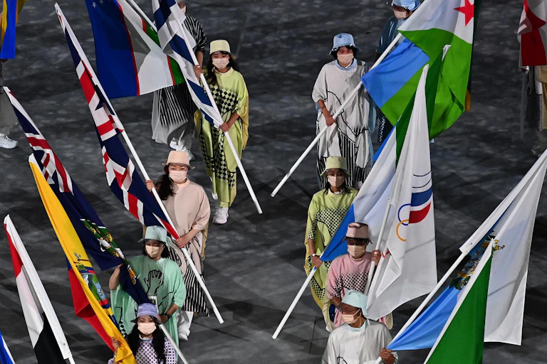 People wearing COVID masks walking into the Olympic stadium in Tokyo carrying national flags.