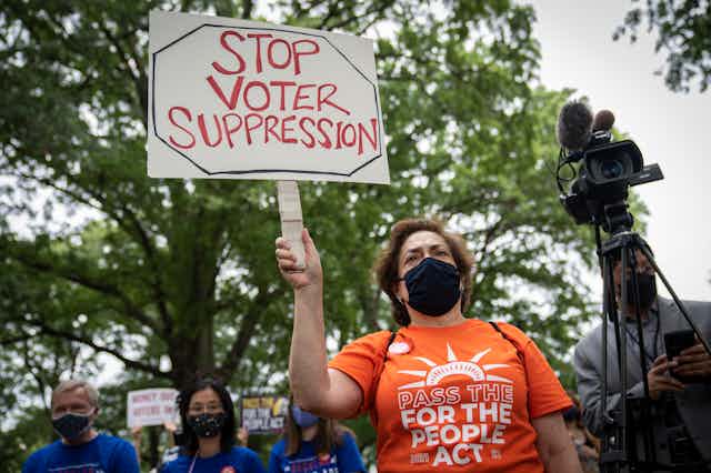A woman in an orange shirt at a rally with a sign that says "Stop voter suppression"