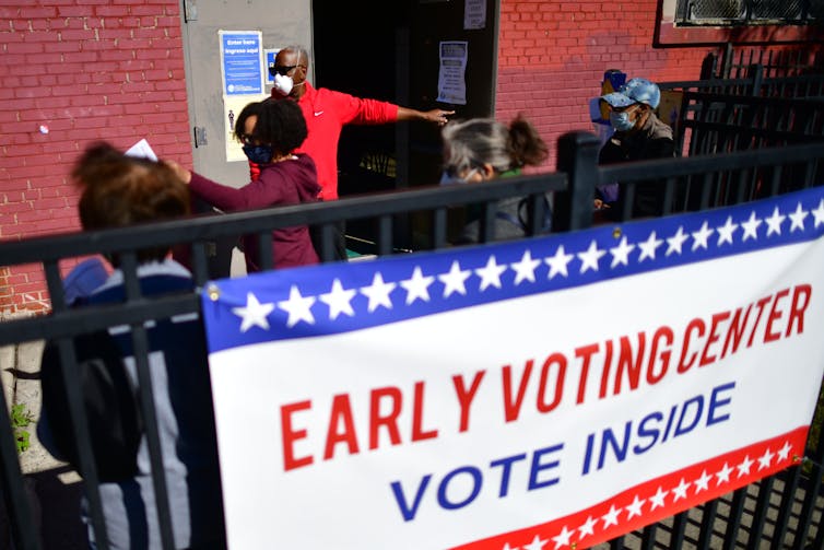 A sign that says Early voting Center with a lot of people standing outside the entrance to the center.