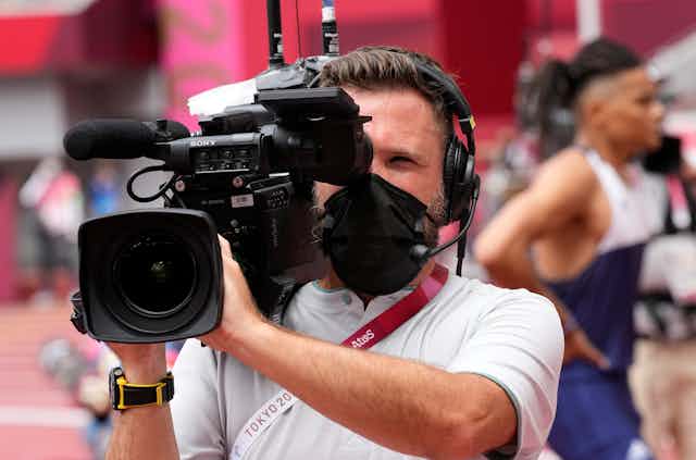 A person holds a broadcast camera setup amid an Olympic event