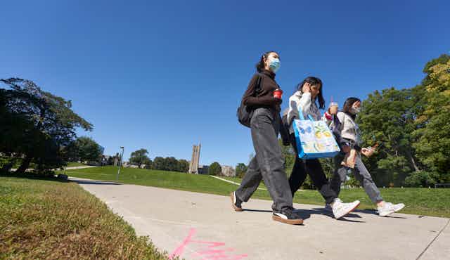 Students walk across a campus wearing face masks.