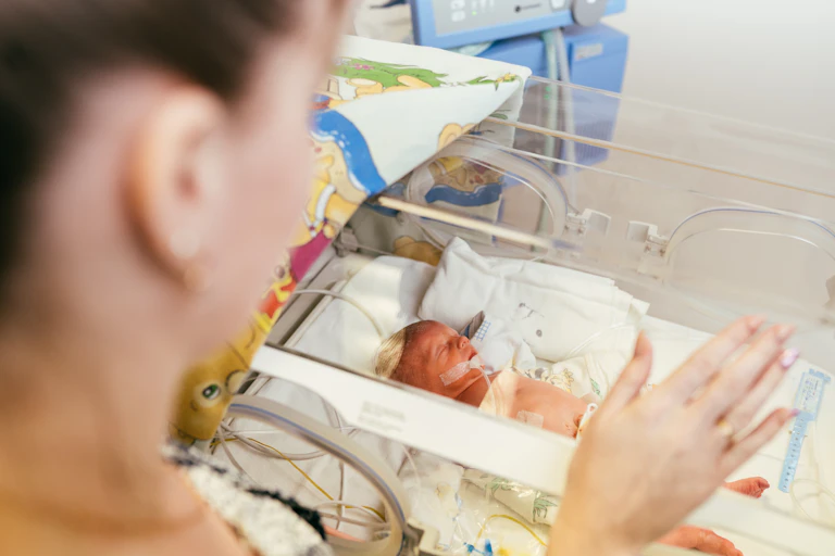 A woman looking at an infant in an incubator