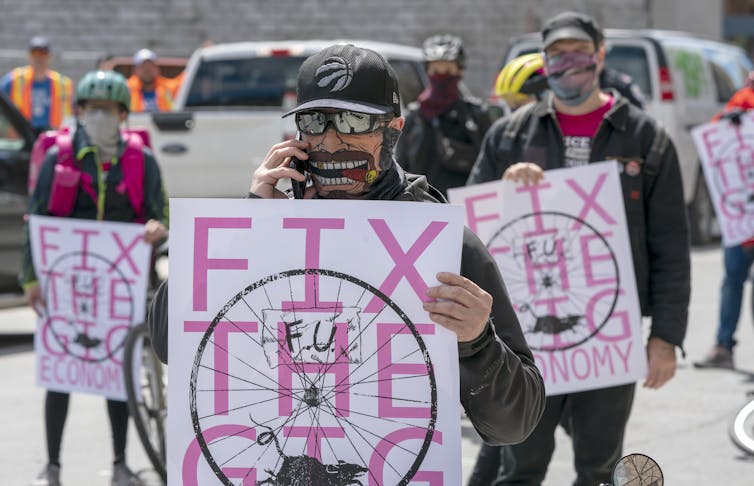 Protestors holding signs saying FIX THE GIG ECONOMY in pink letters on a white background