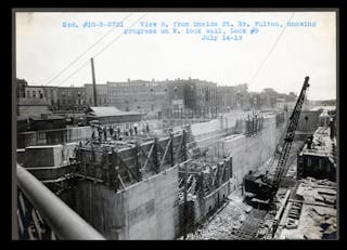 A black and white photo of a construction site, digging a large ditch and working on it with a crane