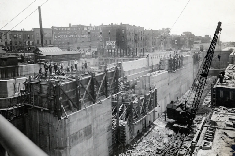 A black and white photo of a construction site, digging a large ditch and working on it with a crane