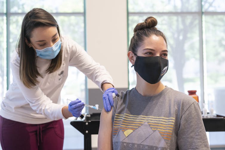 An immunisation nurse vaccinates a young woman.