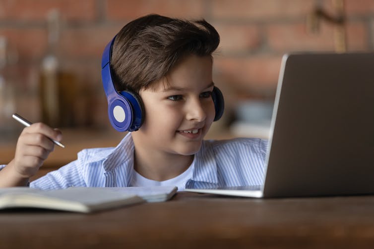 Young boy prepares to write as he talks with someone on his laptop