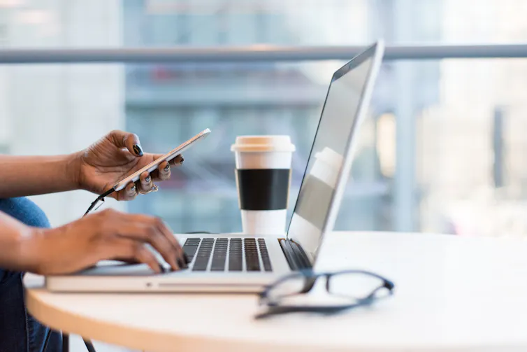Hands using a laptop and smart phone at a desk