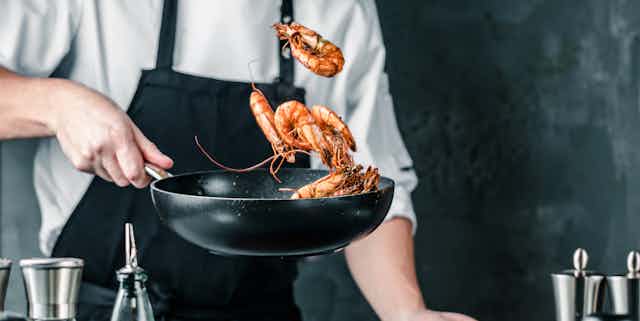 Chef tossing prawns in frying pan. 