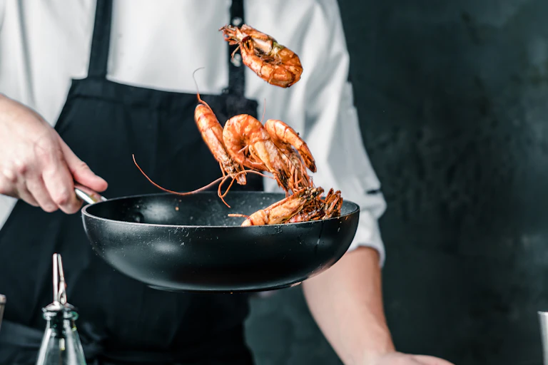 Chef tossing prawns in frying pan.