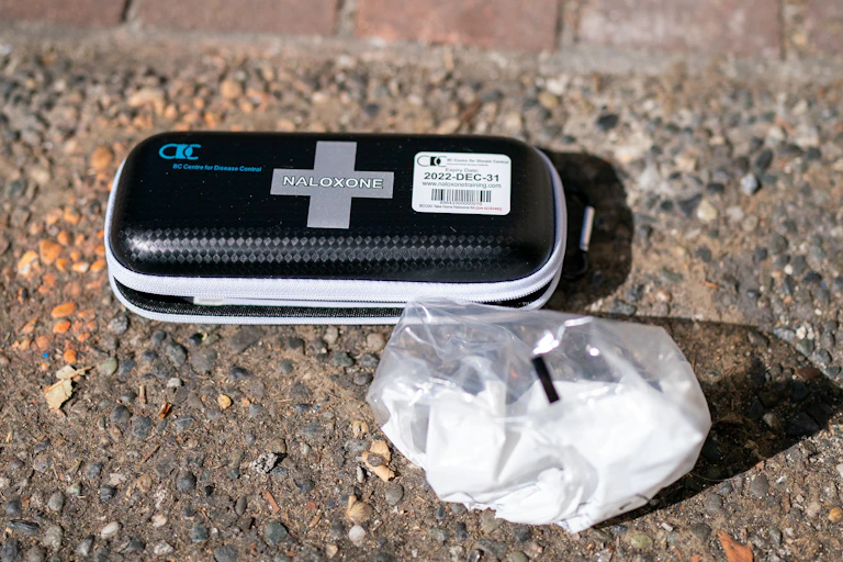 A naloxone kit sitting on the sidewalk, with a bag of white powder