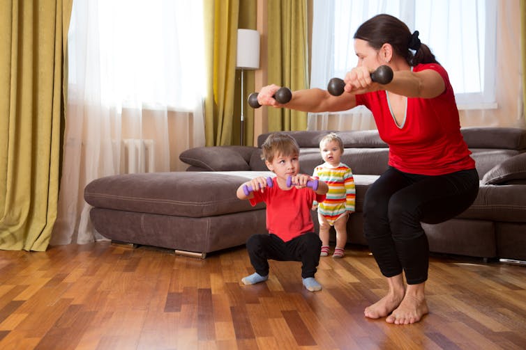A woman does exercise at home with kids.