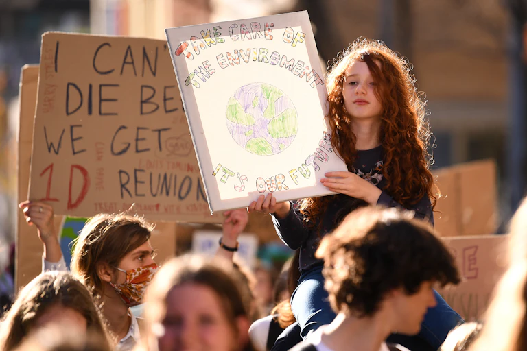 A young girl holds up a sign in a protest that reads 'Take care of the environment it's our future'