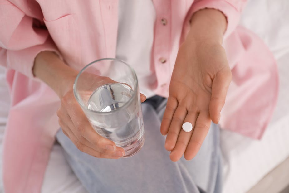 Woman holds a pill in one hand and a glass of water.