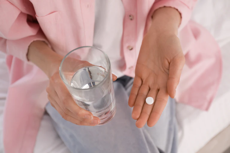Woman holds a pill in one hand and a glass of water.