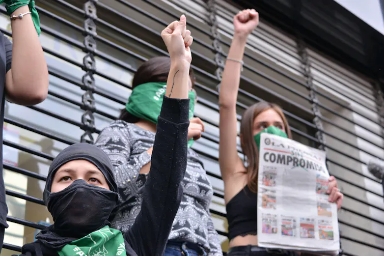 Masked women hold up their fists in protest.