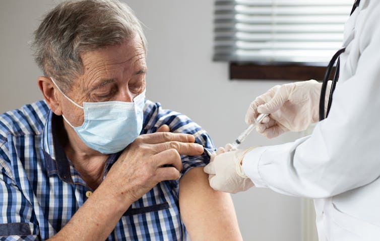 An elderly man in a mask being vaccinated