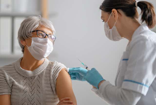 An older woman wearing a mask being vaccinated