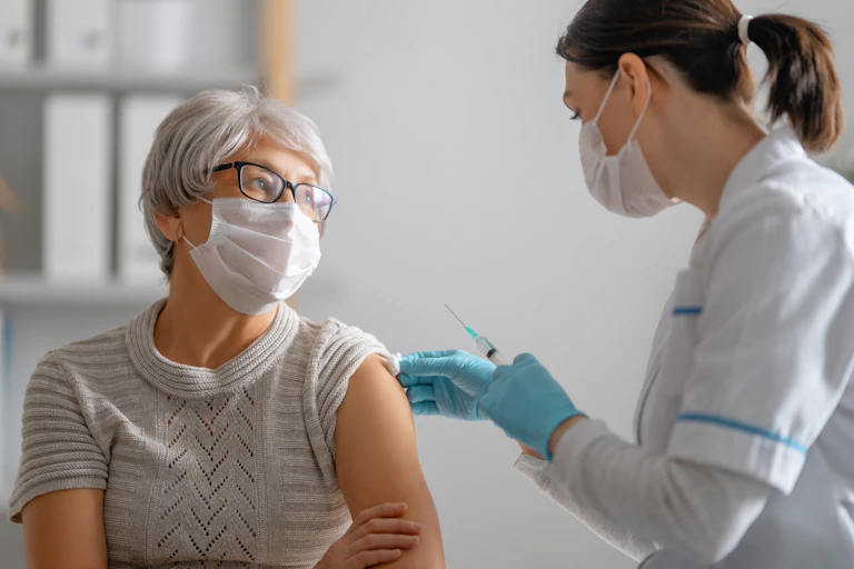 An older woman wearing a mask being vaccinated