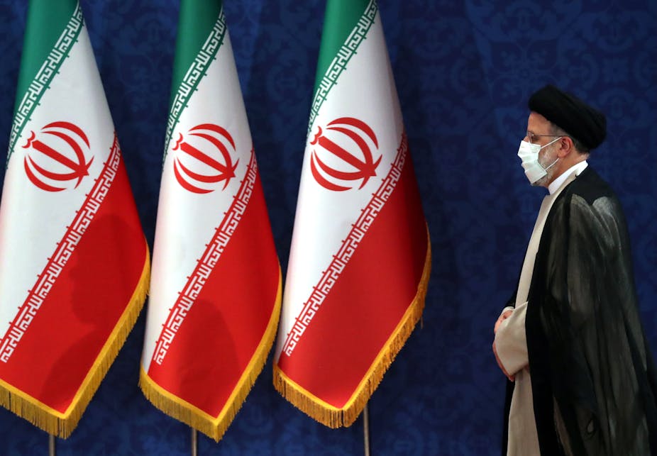 Iranian president, Ebrahim Raisi, wearing a COVID mask walks past an array of Iranian naitonal flags.
