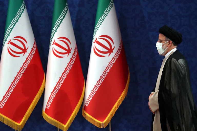 Iranian president, Ebrahim Raisi, wearing a COVID mask walks past an array of Iranian naitonal flags.