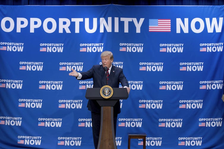 Trump at a podium pointing with an Opportunity Now banner behind him