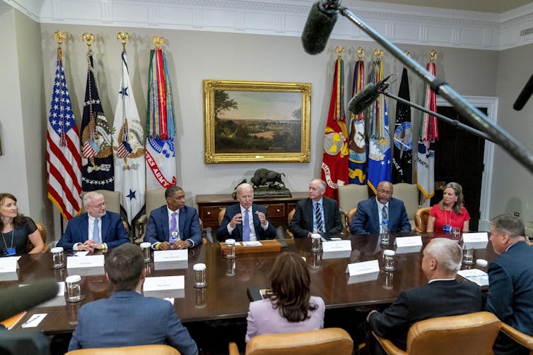 Men and women in business suits sit around a large table.