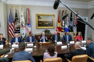 Men and women in business suits sit around a large table.