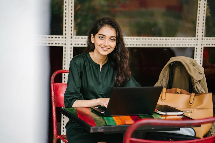 A smiling woman sits behind a laptop.