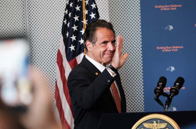 Cuomo stands behind a podium and waves