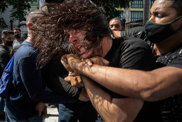 A man with a face mask holds his arms around an unmasked protestor's neck as he pulls him back