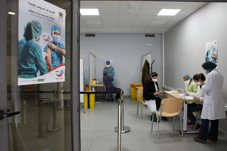 Moroccan doctors wearing masks sit at table table, and a poster encouraging people to get vaccinated hangs on a door in Casablanca, Morocco.