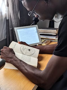 A student at work with a book by a computer screen.