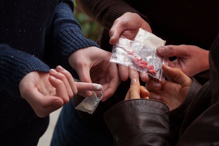 Three pairs of hands holding packets of drugs.