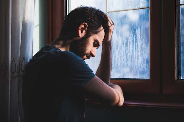 A man leans on a window sill, looking despondent.
