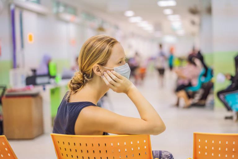Masked woman sits in a hospital waiting room chair.