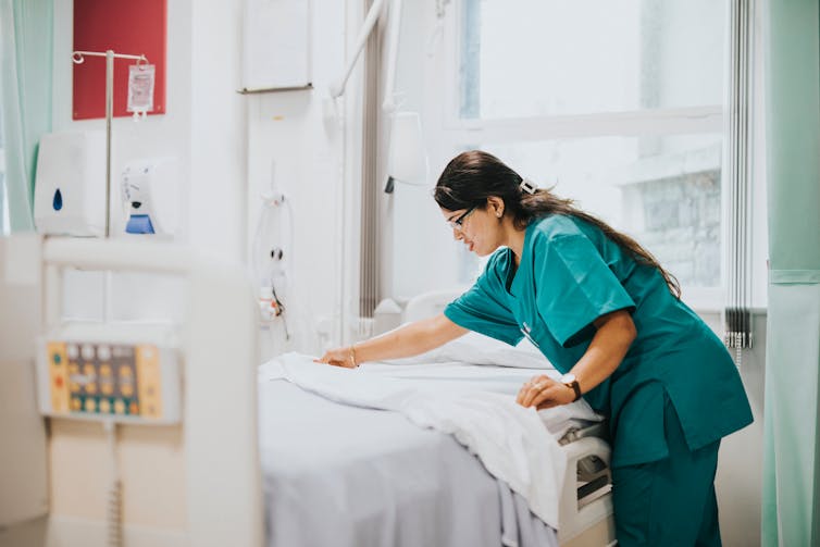 Nurses in scrubs makes a hospital bed.