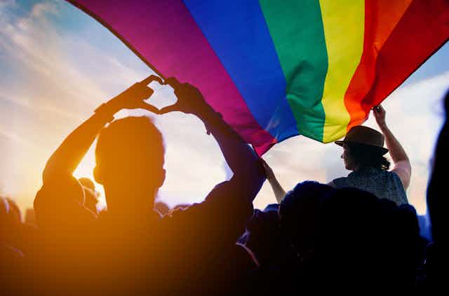 silhouetted people beneath gay pride flag