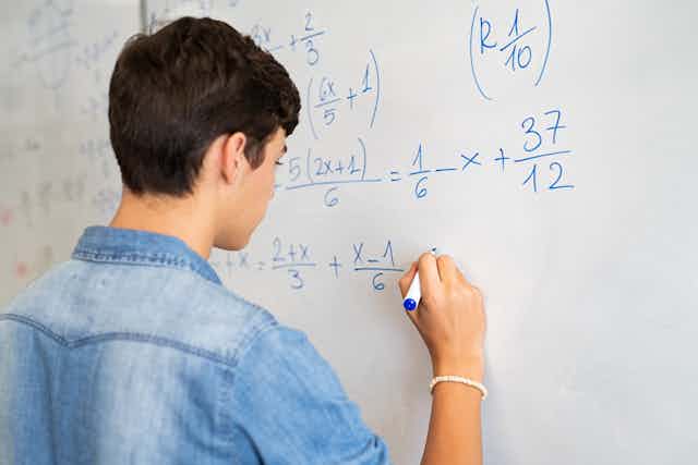 Boy doing maths equations on whiteboard.