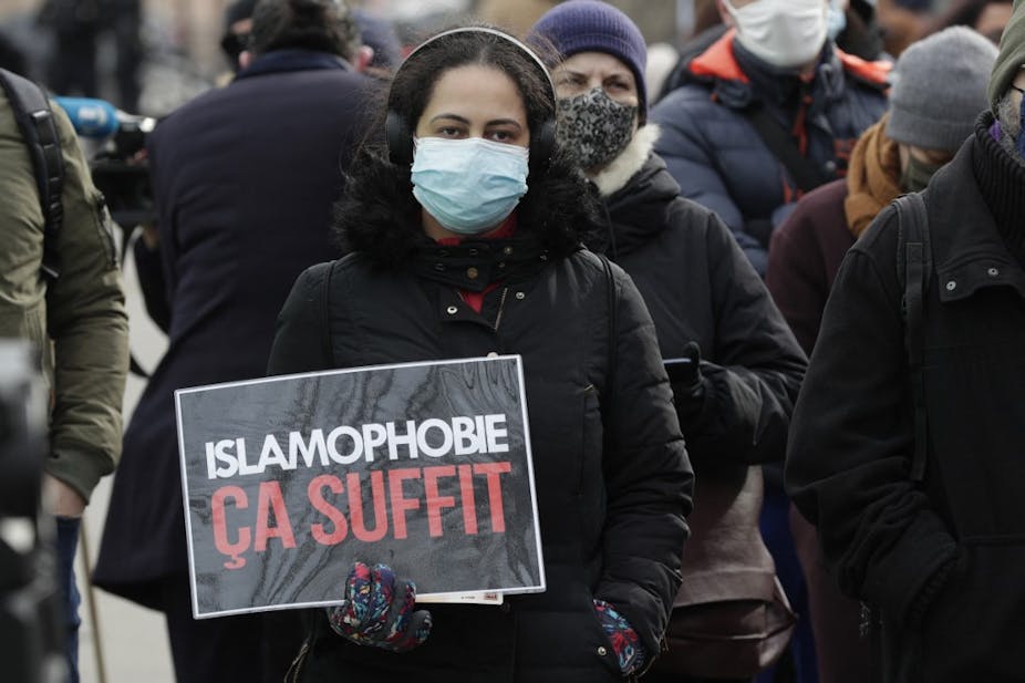 A woman wearing a mask holds a sign in French that reads 'islamophobie ça suffit'.